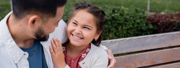 Smiling asian kid hugging father on bench in summer park, banner - foto de stock