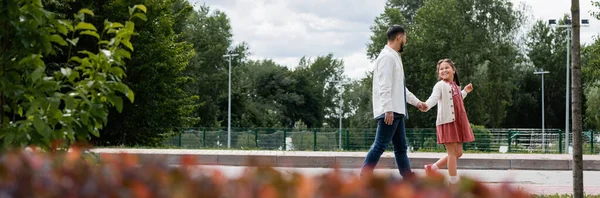 Preteen asian kid holding hand of father while walking in summer park, banner - foto de stock
