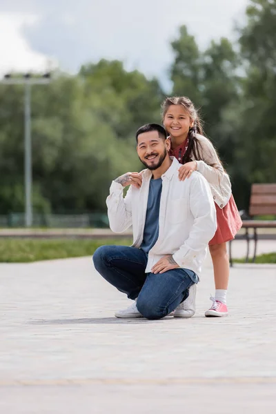 Smiling asian child hugging tattooed father in park - foto de stock