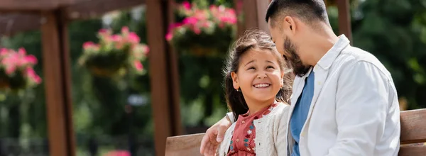 Bearded asian dad hugging daughter on bench in park, banner — Stock Photo