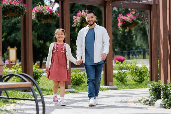 Cheerful asian kid and parent walking and looking at camera in park — Stock Photo
