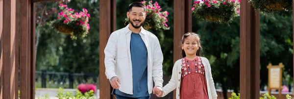 Smiling asian parent and child holding hands while walking in park, banner — Stock Photo