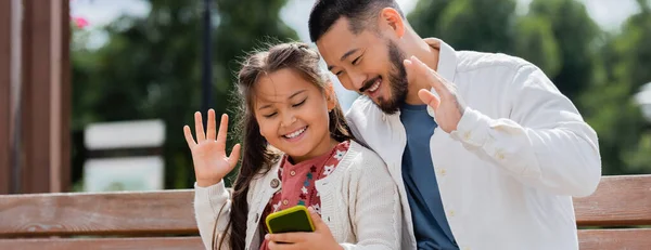 Asian parent and child having video call on smartphone on bench in summer park, banner — Fotografia de Stock