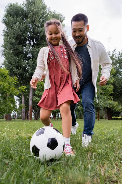 Wide angle view of cheerful preteen girl playing soccer with father in park — Photo de stock
