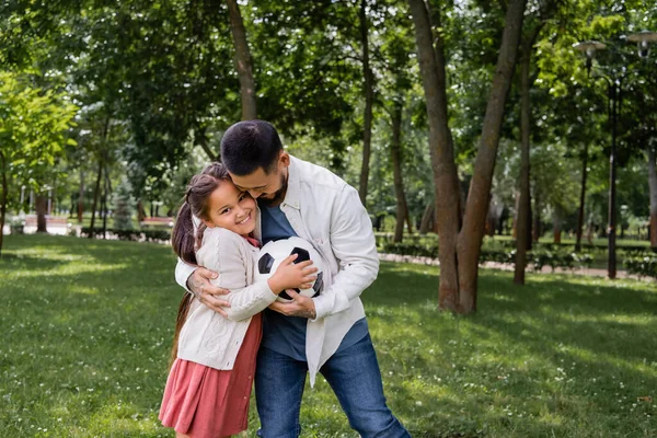 Asian father hugging daughter with football in park — Photo de stock