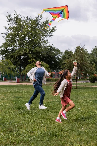 Excited asian dad running near daughter with flying kite in park — Stockfoto