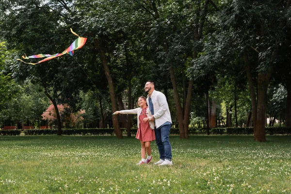 Cheerful asian family looking at flying kite in summer park — Stockfoto