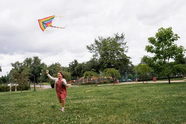 Happy asian girl holding flying kite while running in park — Stock Photo