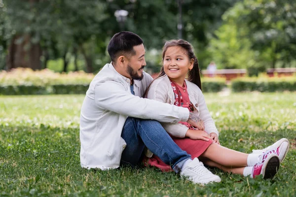 Asian parent hugging happy preteen daughter on grass in park — Stock Photo