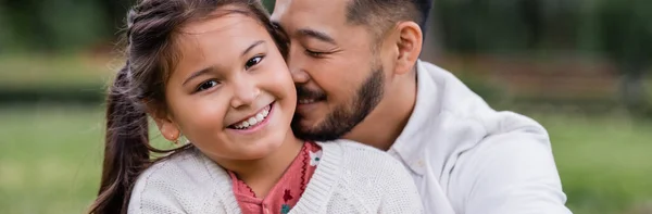 Cheerful asian parent kissing preteen kid in park, banner — Photo de stock