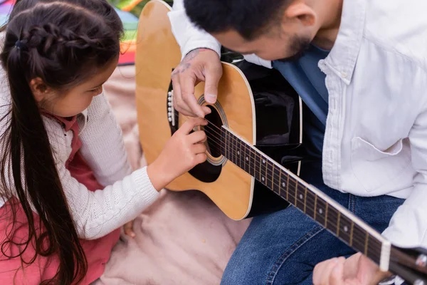 Маленький азиатский ребенок играет на акустической гитаре с отцом на одеяле в парке — стоковое фото
