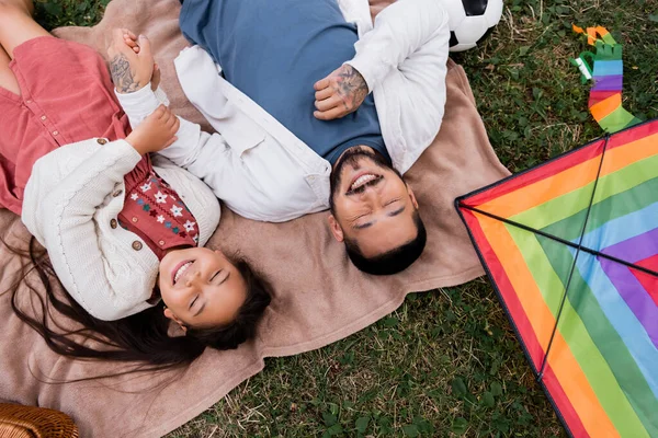 Top view of cheerful asian family holding hands near kite in park — Stock Photo
