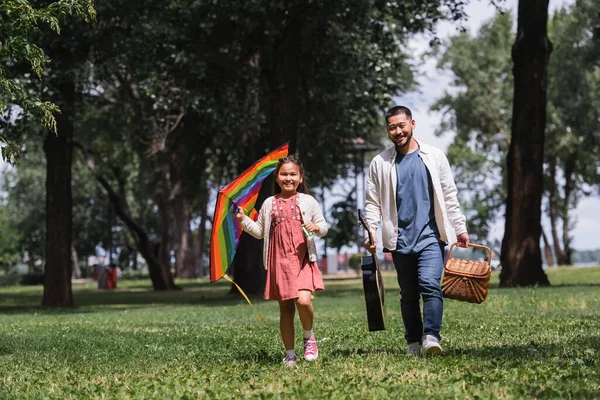 Позитивна азіатська сім'я з літаючим змієм і акустичною гітарою в літньому парку — стокове фото