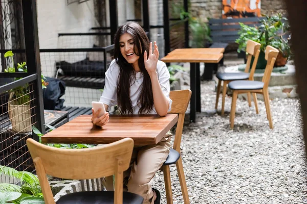 Весела жінка має відеодзвінок на смартфон у кафе на відкритому повітрі — стокове фото