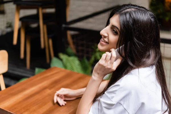 Smiling woman talking on smartphone in outdoors cafe — Stock Photo