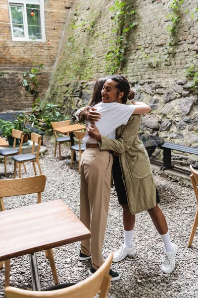 African american woman hugging friend on terrace of cafe — Stock Photo