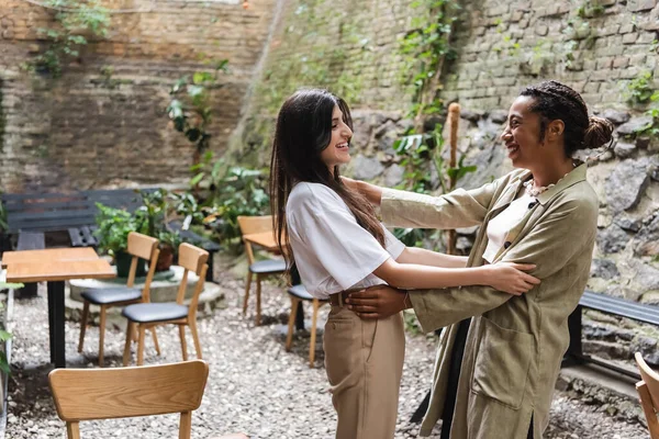 Smiling interracial friends hugging on terrace of cafe — Foto stock