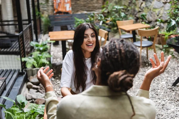 Positive woman looking at blurred african american friend on terrace of cafe — Stock Photo