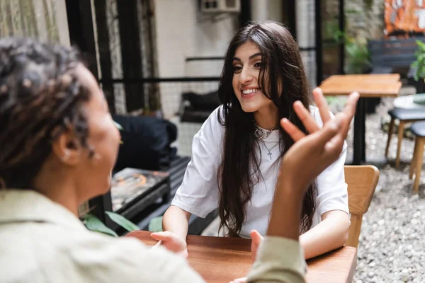 Cheerful woman talking to blurred african american friend on terrace of cafe — Stock Photo