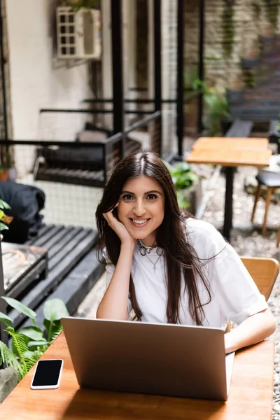 Positive freelancer looking at camera near gadgets on table in outdoor cafe — Foto stock