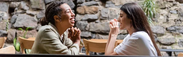 Side view of positive multiethnic girlfriends talking on cafe terrace, banner - foto de stock