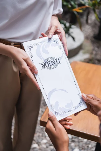 Cropped view of waitress holding menu near african american client on terrace of cafe — Stock Photo