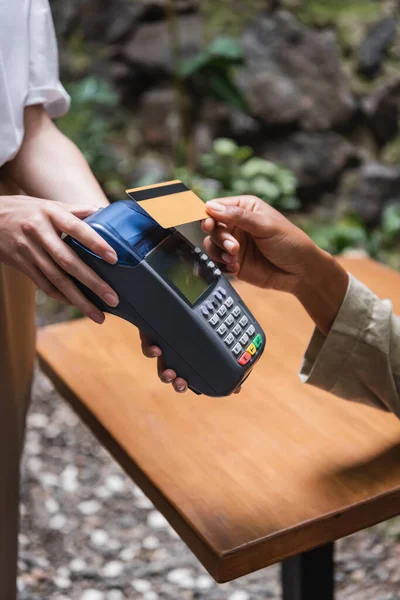 Cropped view of african american woman paying with credit card near waitress in outdoor cafe — Stockfoto