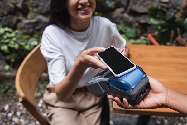 Cropped view of smiling client paying with smartphone near african american waitress in outdoor cafe — Foto stock