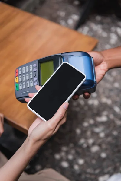 Top view of woman paying with smartphone near african american waitress in outdoor cafe — Stock Photo