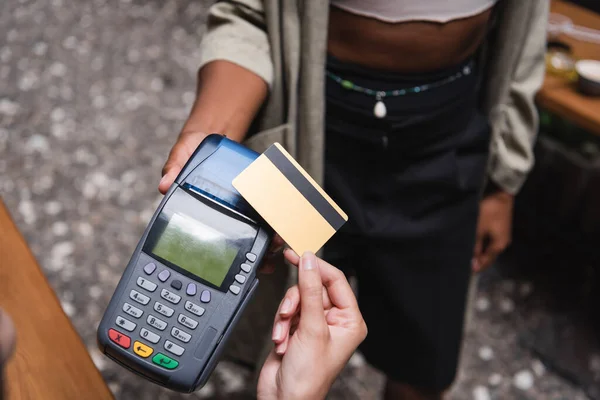 Cropped view of client paying with credit card near african american waitress in outdoor cafe — Stock Photo