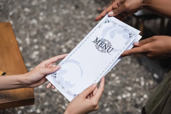 Cropped view of african american waitress holding menu near client on terrace of cafe — Stock Photo