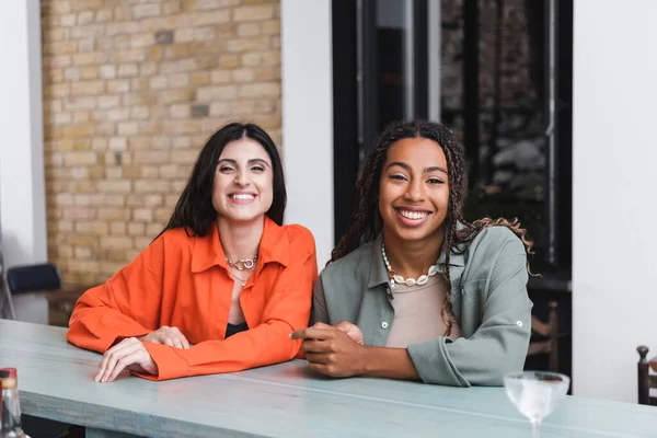 Positive multiethnic friends looking at camera in cafe — Fotografia de Stock