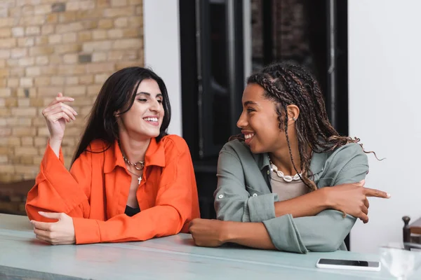 Positive multiethnic girlfriends talking near smartphone in cafe — Foto stock