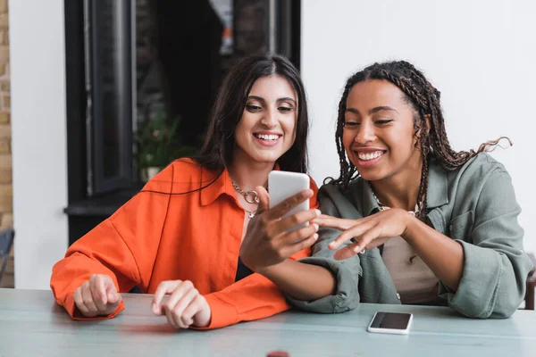 African american woman using smartphone near friend in cafe — Stockfoto