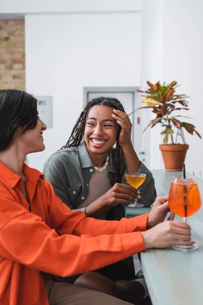 Счастливая американка из Африки держит коктейль и смотрит на подружку в кафе — стоковое фото