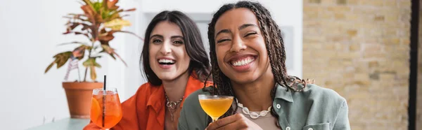 Happy african american woman holding cocktail near girlfriend in cafe, banner — Stock Photo