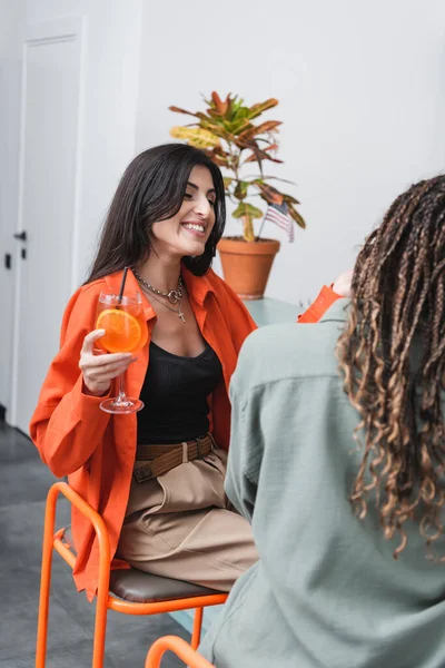 Cheerful woman holding cocktail near african american friend in cafe — Fotografia de Stock