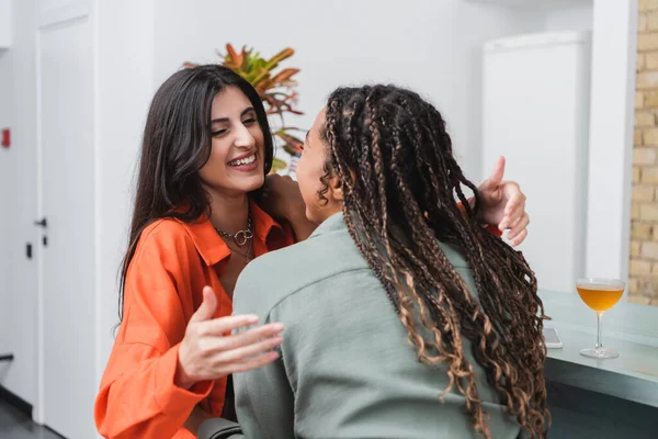 Smiling woman hugging african american friend near cocktail and smartphone in cafe — Stockfoto