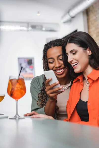 Smiling african american woman using smartphone near friend and blurred cocktails in cafe — Stock Photo