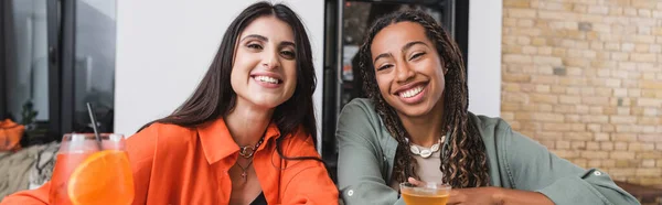 Positive interracial friends looking at camera near cocktails in cafe, banner — Stock Photo