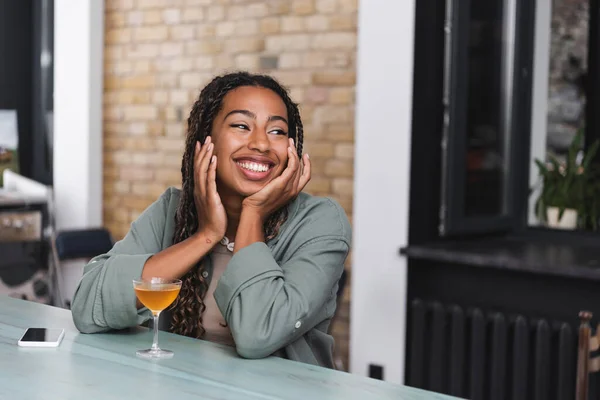 Весела американка-афроамериканка, що дивиться у кафе біля коктейлю і смартфон. — стокове фото