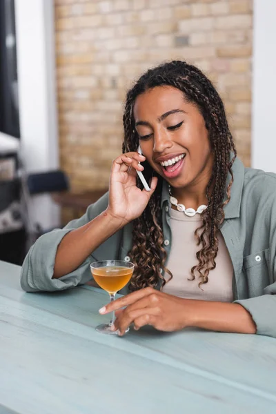 Cheerful african american woman talking on smartphone near cocktail in cafe — Stock Photo