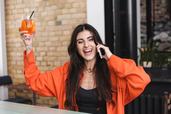 Excited woman holding cocktail and talking on smartphone in cafe - foto de stock