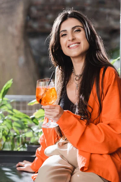 Cheerful brunette woman holding cocktail and looking at camera in cafe — Fotografia de Stock