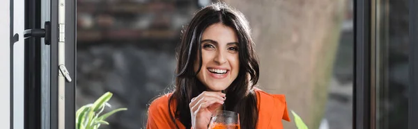 Усміхнена жінка тримає коктейль з питною соломою біля вікна в кафе, банер — стокове фото