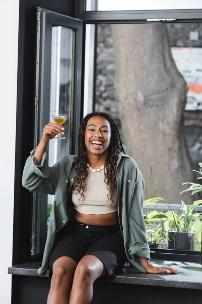 Excited african american woman holding cocktail near window in cafe — Foto stock