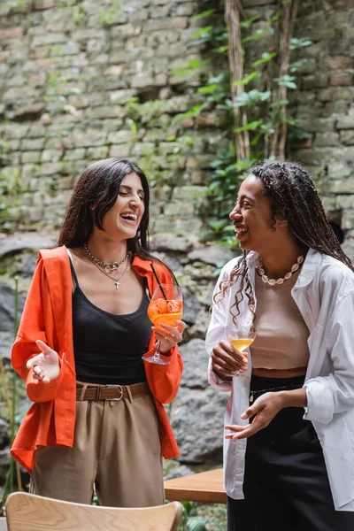 Счастливые многоэтнические друзья разговаривают и держат коктейли на террасе кафе — стоковое фото