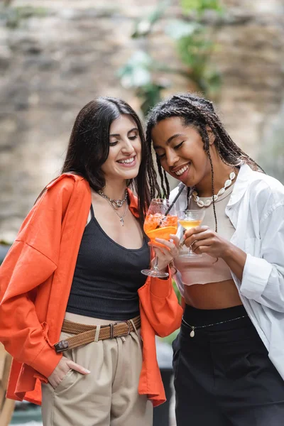 Cheerful multiethnic friends toasting with cocktails on cafe of terrace — Photo de stock