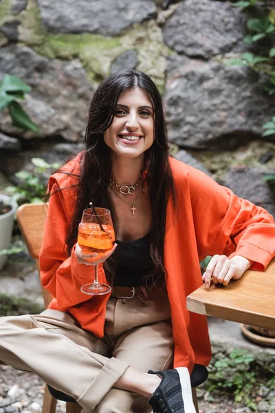 Positive woman holding cocktail and looking at camera on terrace of cafe — Stock Photo