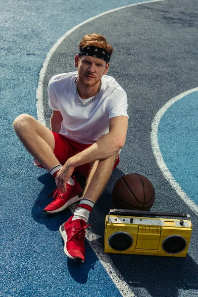 High angle view of young basketball player sitting on court near ball and tape recorder — Photo de stock